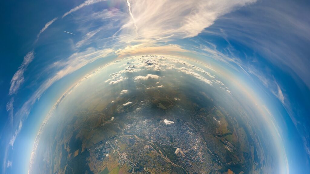 Aerial view from airplane window at high altitude of little planet distant city covered with layer of thin misty smog and distant clouds in evening