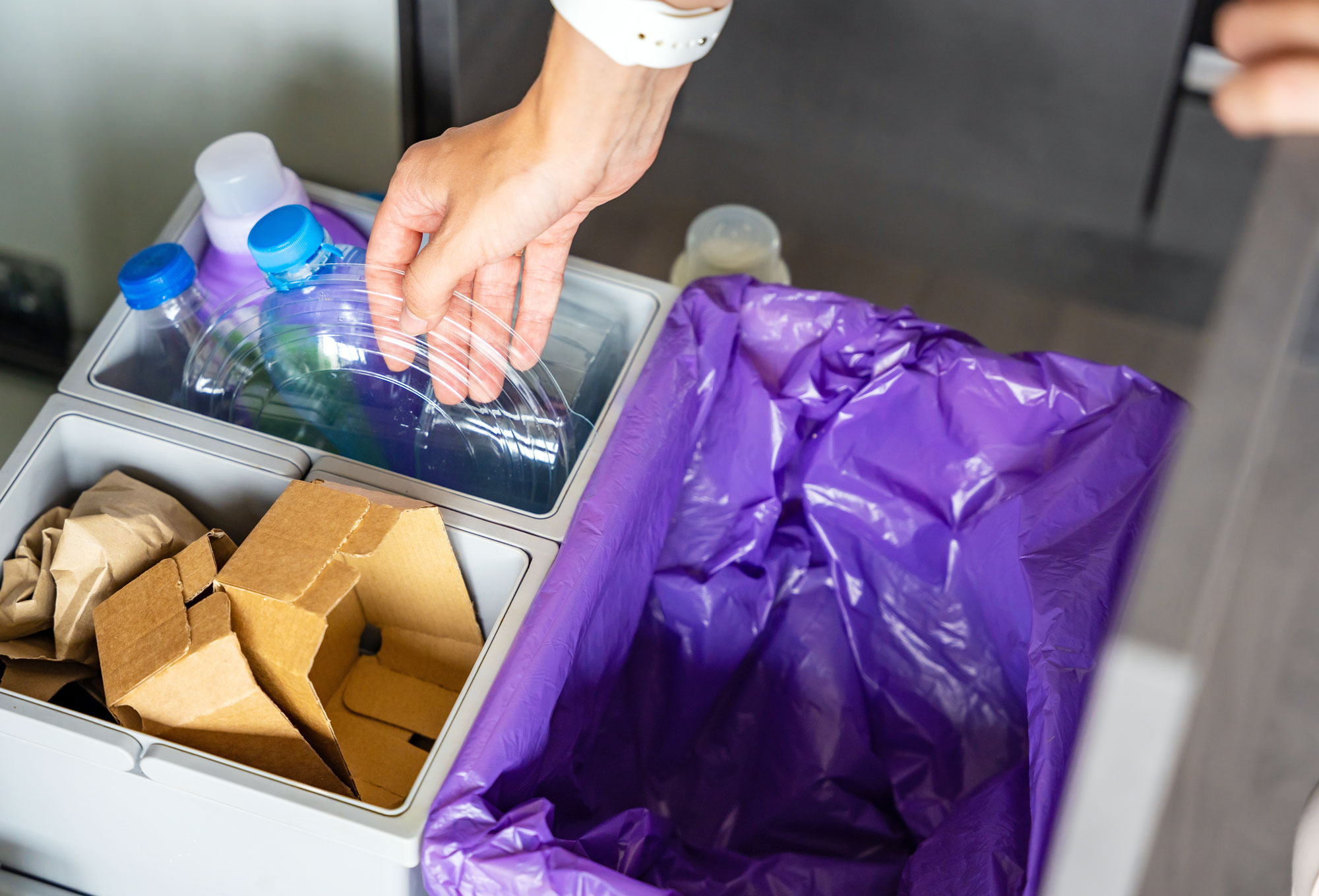 Hand of woman throwing trash into household bins for waste sorting in the kitchen for recycling